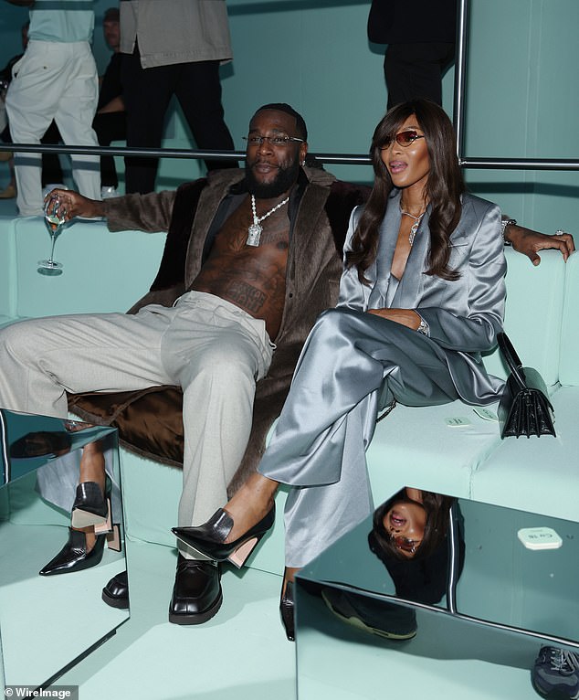 Good form: Naomi accessorised her look with a statement silver necklace as she sat alongside Burna Boy, who went shirtless in white trousers and a long jacket